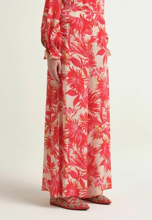 Gonna lunga con motivo floreale rosso acceso indossata con top abbinato a maniche lunghe e scarpe basse con motivo rosso su sfondo chiaro.