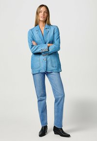 Blazer de mezclilla en azul claro con un diseño estructurado, solapas de pico y bolsillos parche. Combinado con jeans azules a juego y botas de tacón negras.