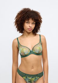 Zelena prozračna temnica s cvetličnim vezenjem v rumeni in roza, ki ima dekorativen osrednji detajl ter ujemajoče se hlačke s podobnimi poudarki.