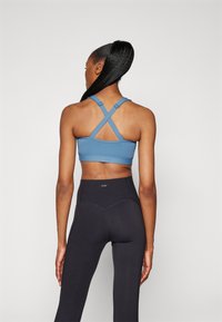 Μπλε σπορ σουτιέν με σχέδιο σταυροειδούς πλάτης, σε συνδυασμό με ψηλόμεσα μαύρα κολάν που διαθέτουν λεπτομέρειες ραφής και λεία υφή.