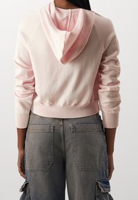 Rosa Kapuzenpullover mit Kapuze, gerippten Bündchen und Saum. Getragen mit grauen Cargohosen mit großen Taschen und lockerem Sitz.