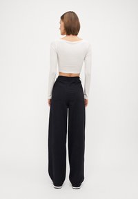 Lys beige cropped langermet topp kombinert med svarte vide bukser. Toppen har en glatt tekstur, og buksene har to baklommer.