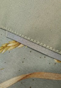 Gros plan de tissu beige texturé superposé à un tissu imprimé avec un motif de blé et de points, montrant des coutures détaillées et des couches de tissu.