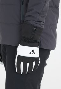 Svart och vit vinterhandske med en texturerad yta, elastisk mudd och dragkedjedetalj. Har en logotyp på handledsområdet.