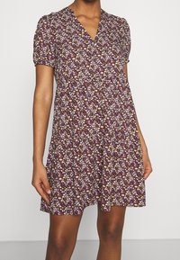 Kurzarmkleid mit lila Blumenmuster und V-Ausschnitt. Aus leichtem Stoff gefertigt, mit lockerer Passform und gerafftem Taillenbereich.