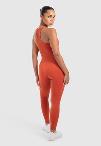Strakke oranje sportoutfit bestaande uit een mouwloze top en een lange legging, met een gladde textuur en een minimalistisch ontwerp.