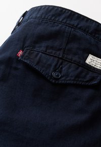 Pantalon Levi's bleu foncé avec une poche arrière boutonnée, un onglet rouge Levi's visible et une étiquette blanche de la marque en haut à droite.