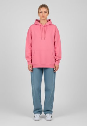 Sweatshirt à capuche rose avec une poche avant et des cordons de serrage, associé à un pantalon texturé bleu clair et des baskets blanches.