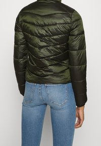 Grön pufferjacka med en figursydd silhuett, med chevron-quiltad design, slät textur och hög krage. Kombination med blå jeans.