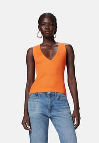 Top arancione a coste senza maniche con scollatura a V profonda, abbinato a jeans blu chiaro. Tessuto liscio con silhouette aderente.