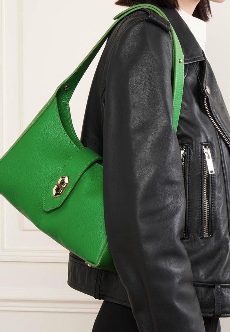 Borsa a spalla in pelle verde con una finitura testurizzata, dotata di chiusura magnetica e dettagli in metallo dorato, indossata sopra una giacca di pelle nera.