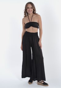 Completo due pezzi nero composto da un top senza spalline con dettagli arricciati e pantaloni a gamba larga con cintura elastica. Indossato con espadrillas nere.