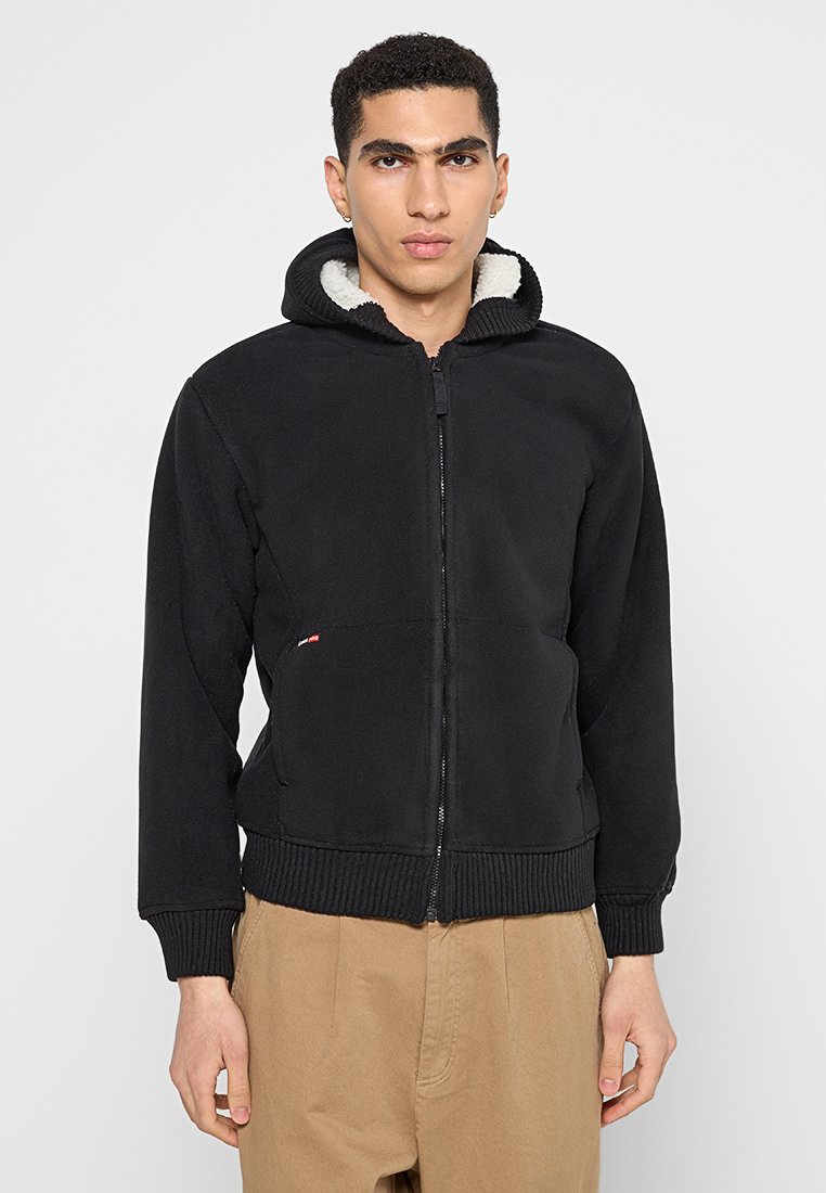 Czarny hoodie na zamek z kapturem wyłożonym futerkiem, ściągaczami przy rękawach i u dołu. Posiada małe logo po lewej stronie. Miękka, teksturowana tkanina.