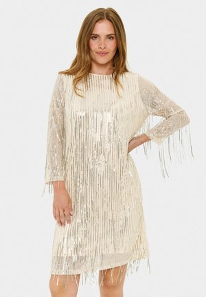 Fransenkleid in Creme mit silbernen Pailletten, runder Ausschnitt und Ärmel in Dreiviertellänge. Fransen hängen von den Ärmeln und dem Saum.