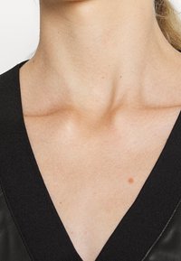 Schwarz V-Ausschnitt-Oberteil mit glatter Textur, das den gut definierten Schlüsselbeinbereich und den Hautton betont, minimale sichtbare Details.