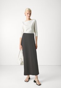 Witte top met lange mouwen, grijze geribbelde maxi rok, sandaaltjes met blokhak en een kleine witte handtas.