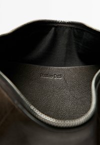 Open donkerbruine leren tas met zwarte stoffen voering en zilveren rits, met een opgeblazen ‘Massimo Dutti’ logo aan de binnenkant.