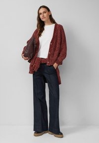 Roter Strickcardigan mit großen Knöpfen, getragen über einem weißen Hemd, kombiniert mit dunkelblauen Jeans und beigen Plateauschuhen. Braune Tasche getragen.