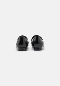Mocassins en cuir noir avec une finition brillante, un petit talon empilé et des découpes arrondies sur les côtés. Texture lisse et design minimaliste.