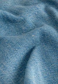 Gros plan d'un tissu en denim bleu clair montrant la texture détaillée du tissage et des plis doux.