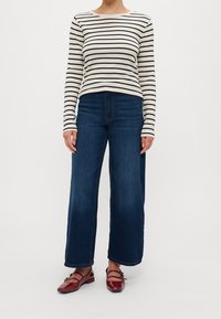 Gestreiftes Langarmoberteil in Creme und Marine, kombiniert mit dunkelblauen weiten Jeans. Rote Lacklederballerinas mit zwei Schnallenakzenten.
