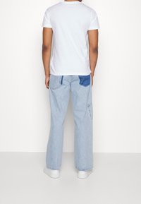 White t-shirt, short sleeves, paired with light blue denim cargo pants featuring a patch of darker blue, and white sneakers.