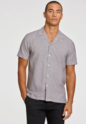 Camisa corta de manga corta gris claro con cuello con muesca, tejido texturizado y botones en la parte delantera. Se lleva con pantalones negros, de corte casual.