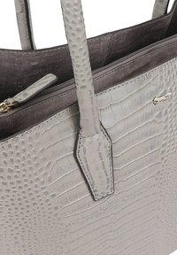 Lichtgrijze tote bag van faux krokodillen-embost materiaal met gestructureerde hengsels, een ritsvak en een zilveren logo-accent.