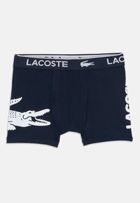 Sötétkék boxer sort fehér krokodil grafikával a bal oldalon és "LACOSTE" felirattal függőlegesen, fehér színben a jobb oldalon. Rugalmas anyagból készült.