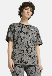 Camiseta de manga corta con patrón de camuflaje gris, con un borde negro y un pequeño logotipo blanco en el lado izquierdo. Hecha de una tela suave y texturizada.