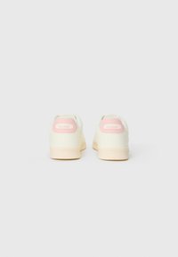 Sneaker bianche con dettagli rosa chiaro e branding sul tallone, caratterizzate da un materiale superiore liscio e una suola testurizzata.