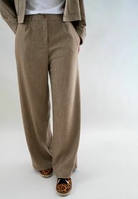 Bruine, gestructureerde wijde broek met twee voorzakken en een knoopdetail bij de taille, gecombineerd met sneakers met luipaardprint.