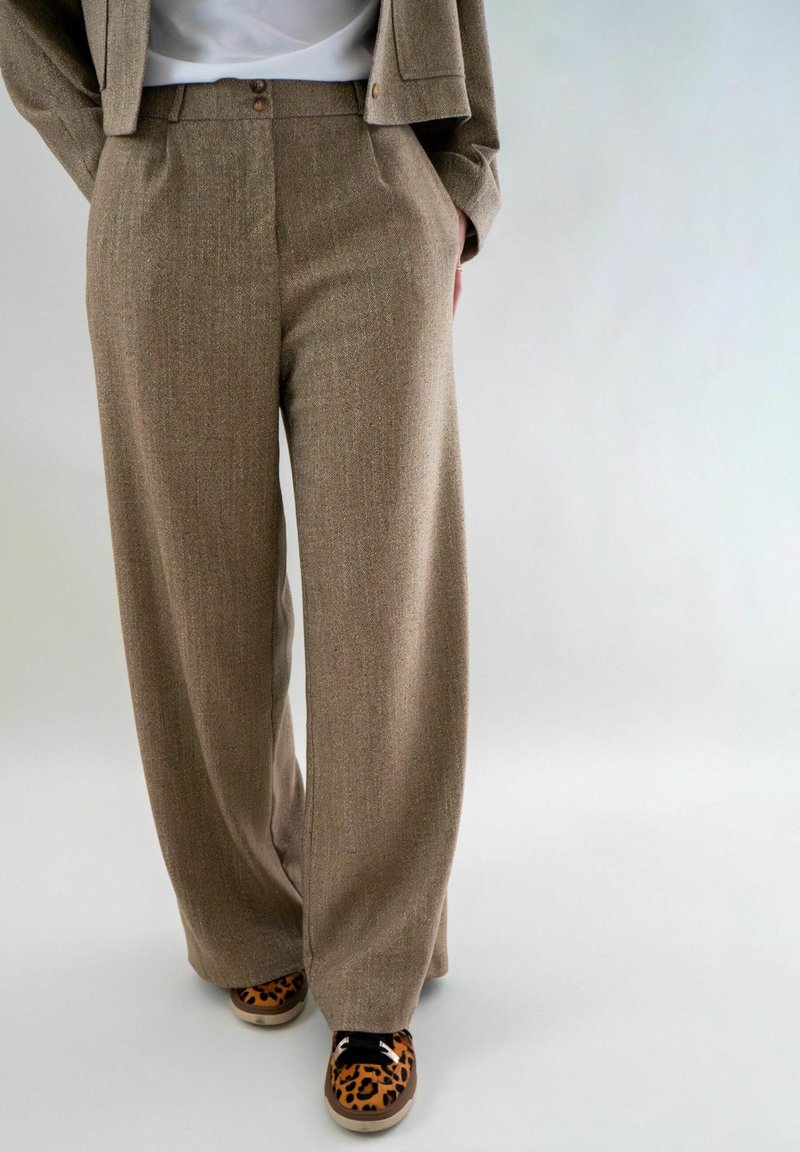 Bruine, gestructureerde wijde broek met twee voorzakken en een knoopdetail bij de taille, gecombineerd met sneakers met luipaardprint.