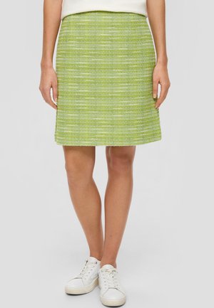 Jupe évasée en tweed vert avec une surface texturée, arborant des rayures horizontales de teintes plus claires, associée à des baskets blanches.