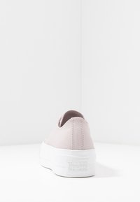 Zapatilla de cuero rosa claro con una suela de goma blanca, que presenta un diseño de corte bajo y costuras texturizadas, mostrando el logo "Converse All Star".