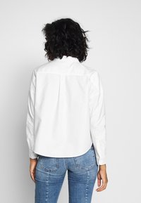 Vit, skjortkragig, knäppning upp skjorta med långa ärmar, strukturerad design och rundad nederkant. Matchas med åtsittande blå denimjeans.