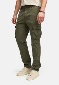 Pantalones cargo verde oliva con múltiples bolsillos laterales y corte recto, fabricados en resistente tejido de algodón, combinados con zapatillas de color claro.