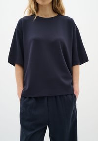 Sötétkék, oversize póló, puha anyagból készült, rövid ujjú és kerek nyakkivágású, sötét, szabott nadrággal párosítva.