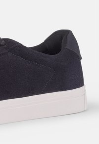 Navy blue suede low-top sneaker with a white rubber sole, featuring smooth texture and seamless design at the heel.