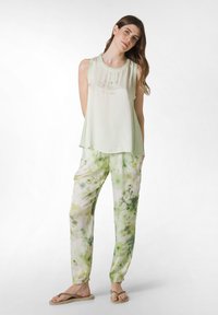 Lys grøn tanktop med tekst, parret med løse, mønstrede bukser i grønne og hvide nuancer. Blødt stof, afslappet pasform og simple flip-flops.