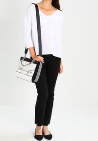 Svart och vit handväska med strukturerad design, metalliska detaljer och kontrasterande ränder. Används som en korsväska med en slät, läderliknande textur.