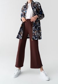 Granatowa kurtka w kwiatowy wzór z zamkiem, biała koszulka, brązowe spodnie z szerokimi nogawkami i białe sneakersy. Wyrazisty nadruk kwiatowy i luźny krój.