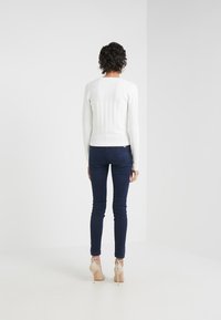 Biała sweter o prążkowanej fakturze, w komplecie z ciemnoniebieskimi rurkami i cielistymi szpilkami, podkreślająca dopasowaną sylwetkę i teksturowany materiał.