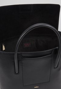Svart läder tote-väska med slät textur, två handtag och ett fack med dragkedja invändigt. Har en guld "Furla"-logotyp och ett textilfoder.