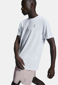 Weißes kurzärmliges T-Shirt mit subtiler Logo-Platzierung auf der Brust, kombiniert mit pinken Sportshorts, die einen diagonalen Schnitt und Logo-Details aufweisen.