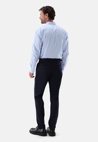 Camicia da uomo a righe azzurro chiaro abbinata a pantaloni blu navy, con vestibilità su misura e dettagli di bottoni discreti. Scarpe nere completano il look.