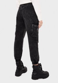 Svarta cargo-byxor med elastiska ärmslut och en urblekt textur, med sidofickor och dragkedjedetaljer, kombinerat med kraftiga svarta kängor.