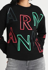 Černá mikina s odvážným, vícebarevným nápisem "ARNANI" v červené, zelené a modré barvě, s kulatým výstřihem a dlouhými rukávy.