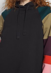 Felpa con cappuccio con corpo nero e maniche raglan multicolori in verde, beige, bordeaux, arancione e rosa chiaro; tessuto morbido, dettaglio con coulisse.