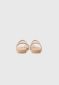 Beige kumisaappaat, joissa on minimalistinen muotoilu. Kaksi ohutta hihnaa ja litteä pohja. Yksinkertainen ilman koristeita, ainoastaan hienovarainen logo kantapäässä.